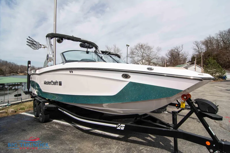 Slide: The Image of 2024 MasterCraft XT24 boat on trailer, white and teal, parked outdoors. - 0