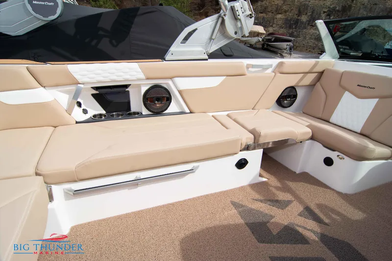 Slide: The Image of 2024 MasterCraft XT24 boat interior with beige and white seating, speakers, and cup holders. - 19