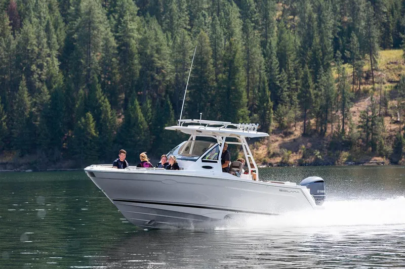 Slide: The Image of 2024 Solara 250 CW boat cruising on a scenic lake with forested background. - 2