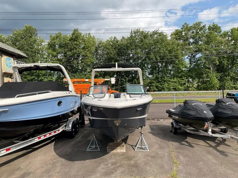 Slide: The Image of 2024 Chaparral 250 OSX boat displayed outdoors with jet skis nearby. - 3