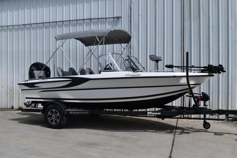 The Image of 2024 Triton 186 Allure boat with canopy on trailer, parked by metal building. - 0