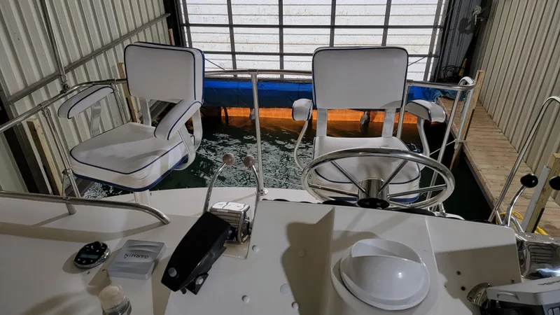 Slide: The Image of 1983 Bertram 33 Flybridge Cruiser helm with white captain chairs in a boat dock. - 10