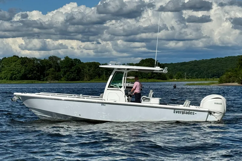 Slide: The Image of 2024 Everglades 273 Center Console boat cruising on a lake with lush green shoreline. - 7