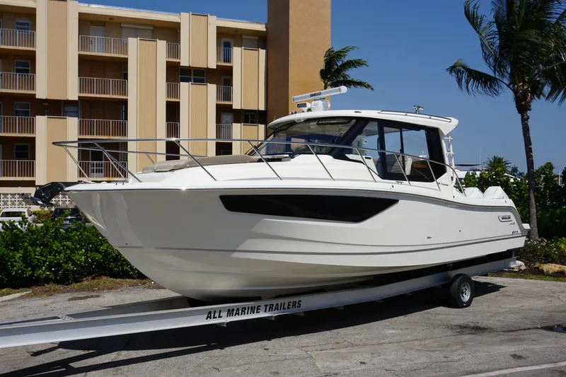 Slide: The Image of 2025 Boston Whaler 365 Conquest boat on trailer, parked near a building and palm trees. - 10