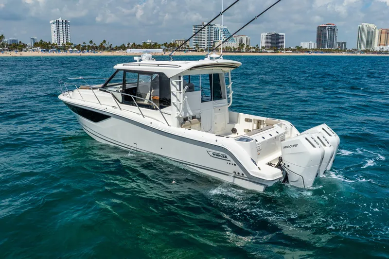 Slide: The Image of 2025 Boston Whaler 365 Conquest boat cruising near a city shoreline. - 2
