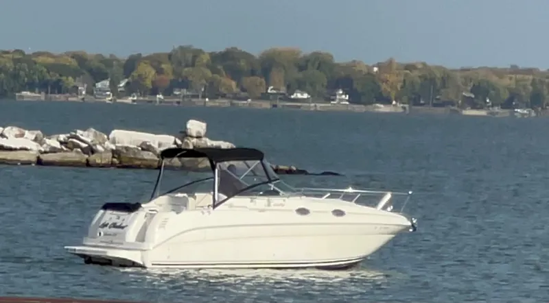 Slide: The Image of 2001 Sea Ray 260 Sundancer boat on calm water near rocky shore and wooded background. - 15