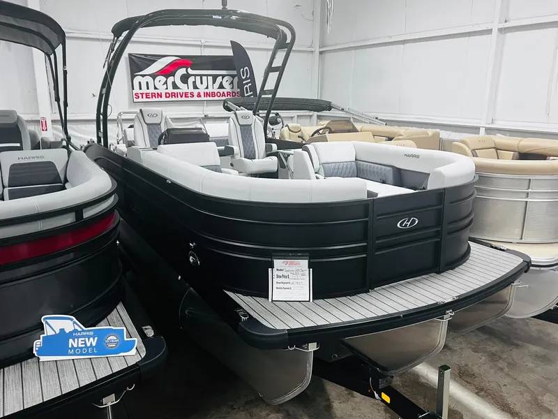 Slide: The Image of 2024 Harris Sunliner 250 Sport pontoon boat in showroom, featuring sleek black design and spacious seating. - 18