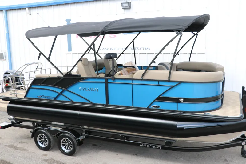 Slide: The Image of 2025 Sylvan Mirage X3 CLZ DH pontoon boat with blue and black design on a trailer. - 14