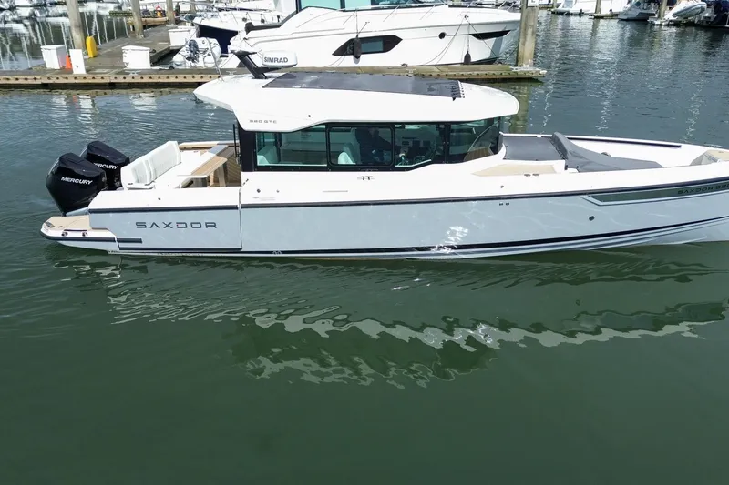 Slide: The Image of 2026 Saxdor 320 GTC boat docked in marina, featuring sleek design and twin Mercury engines. - 25