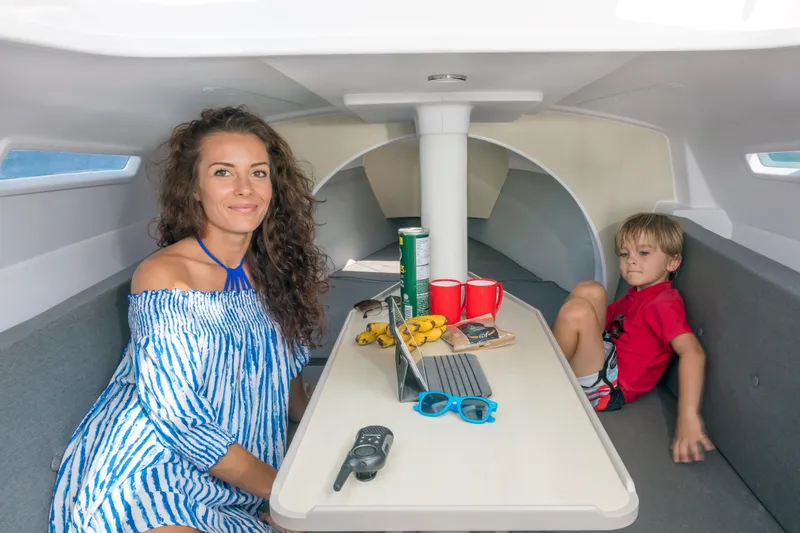Slide: The Image of Family relaxing inside a 2026 Corsair 760 sailboat cabin with snacks and a laptop. - 32