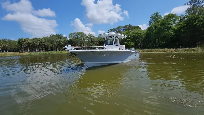 Slide: The Image of 2023 Sea Hunt Gamefish 27 boat on calm water with lush green shoreline. - 26