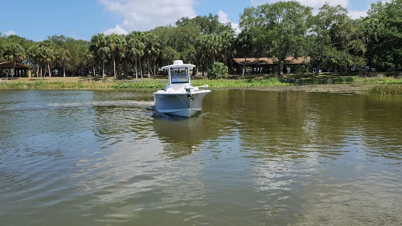 Slide: The Image of 2023 Sea Hunt Gamefish 27 boat cruising on a calm lake near a wooded shoreline. - 48