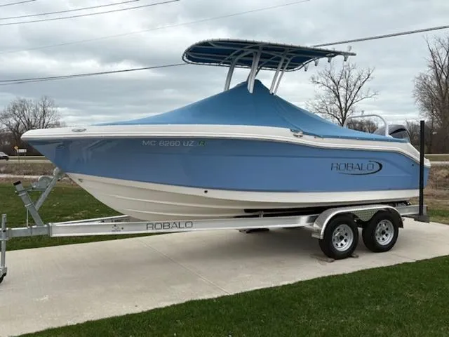 Slide: The Image of 2024 Robalo R202EX boat on trailer, blue cover, parked outdoors. - 13