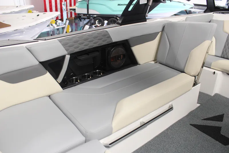 Slide: The Image of 2024 MasterCraft XT24 boat interior with gray and beige seating, cup holders, and speaker system. - 23