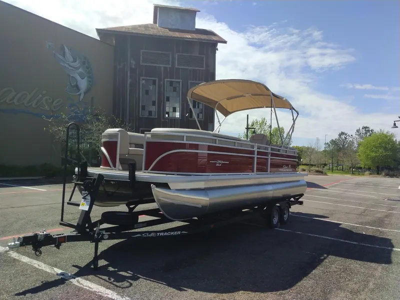 Slide: The Image of 2024 Sun Tracker Party Barge 24 DLX pontoon boat on trailer in parking lot. - 2