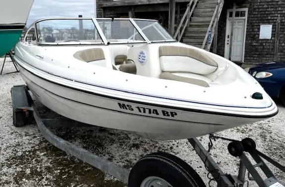 The Image of 2005 Glastron MX boat on trailer, white exterior, parked outdoors near wooden building. - 0