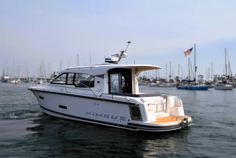 Slide: The Image of 2024 Nimbus 305 Coupe yacht on calm water with marina background. - 2