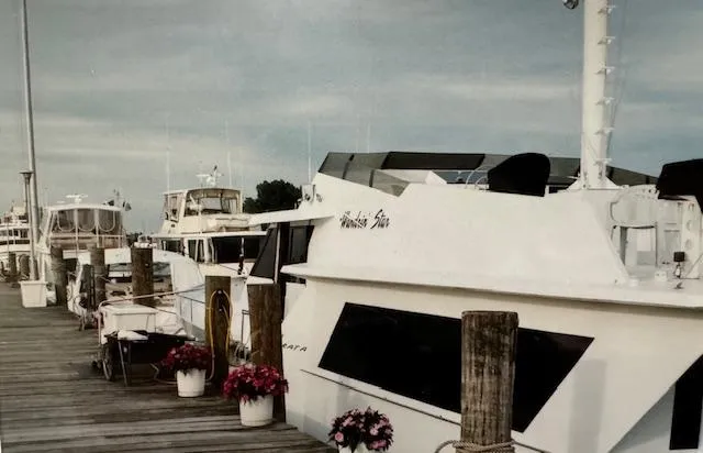 Slide: The Image of 1990 Motor Yacht 70 Brata docked, surrounded by other boats and potted flowers. - 5