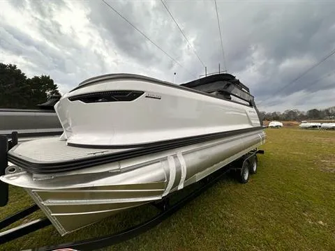 The Image of 2024 Manitou 24 Explore pontoon boat on a trailer under cloudy skies. - 0