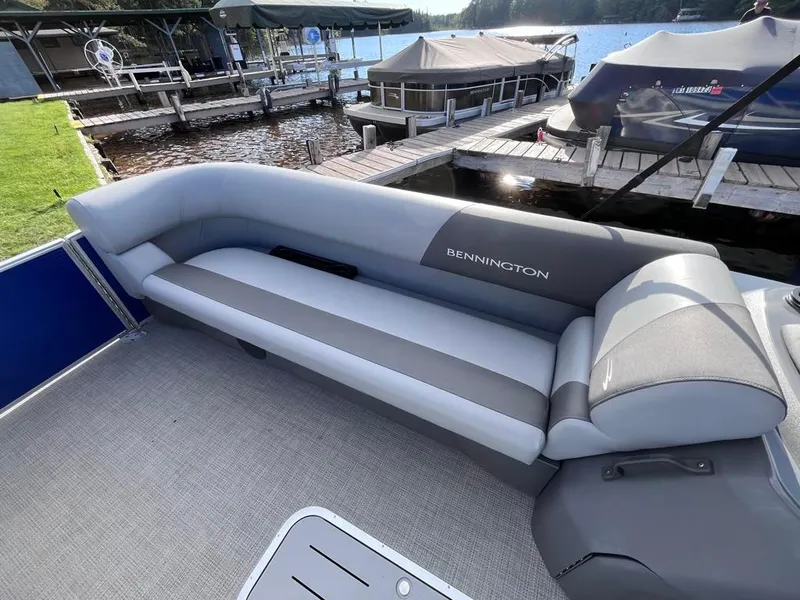 Slide: The Image of 2024 Bennington 22SVL-SPS pontoon boat interior with gray seating at a lakeside dock. - 10