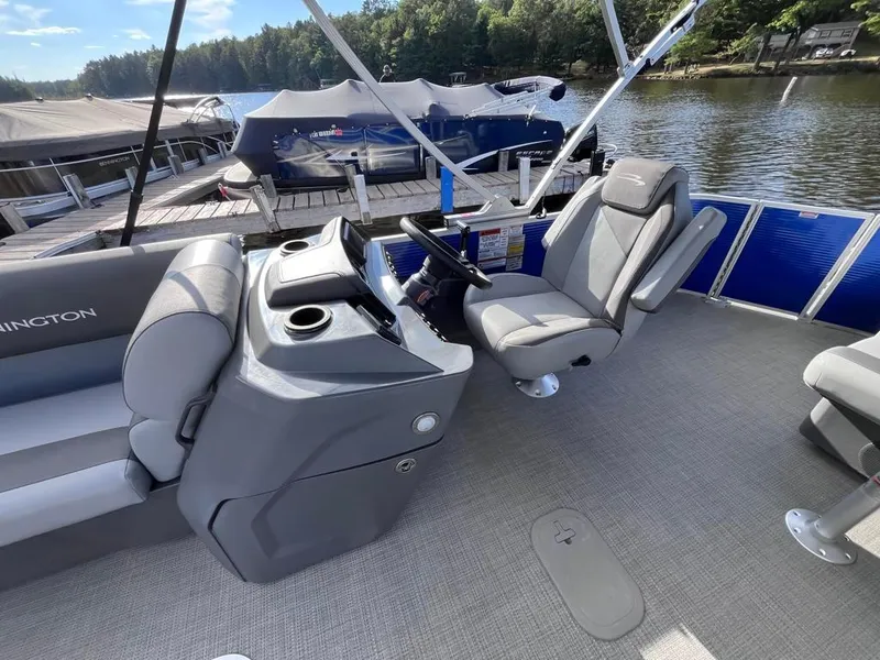 Slide: The Image of 2024 Bennington 22SVL-SPS pontoon boat interior with helm and seating by a lake. - 16