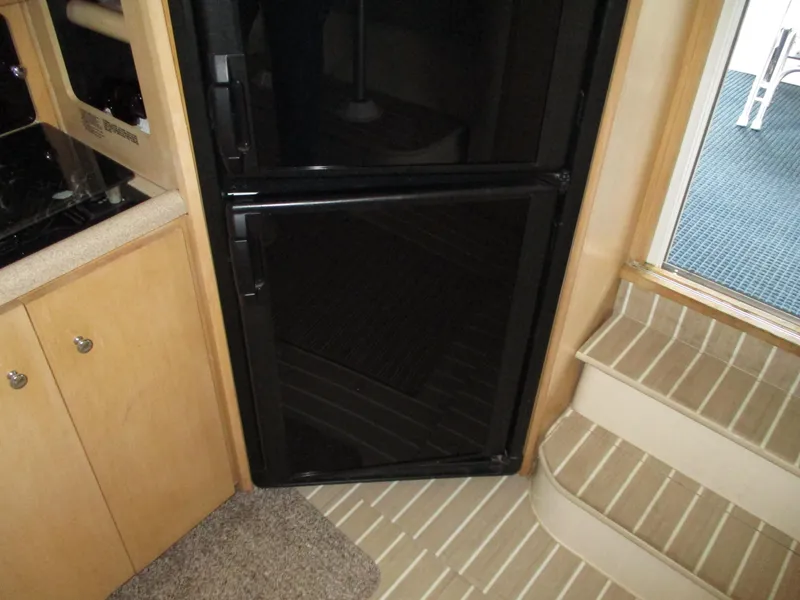 Slide: The Image of 1997 Carver Voyager interior with black fridge, wooden cabinets, and striped flooring. - 27