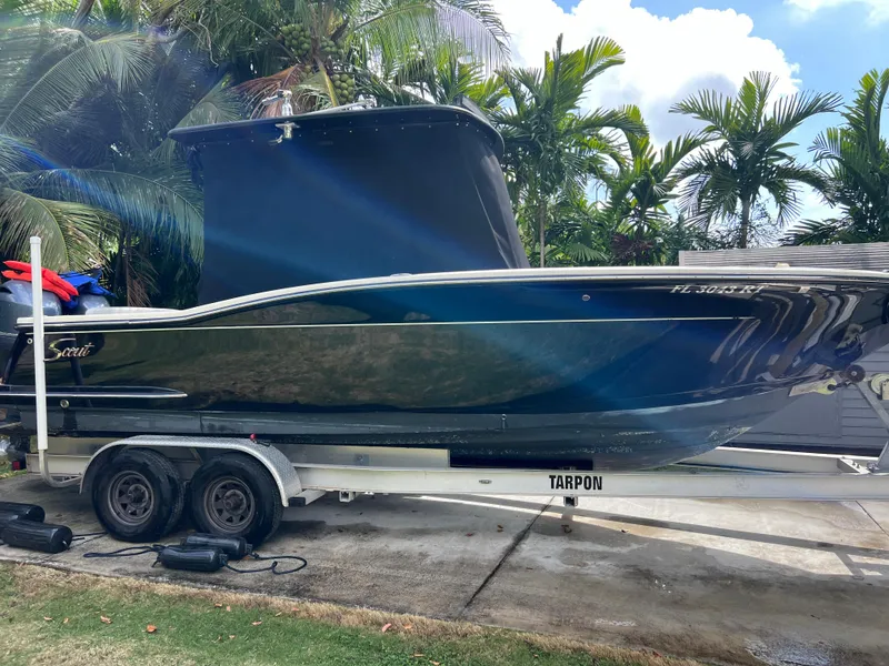 Slide: The Image of 2019 Scout 255LXF boat on a trailer, surrounded by tropical plants. - 12