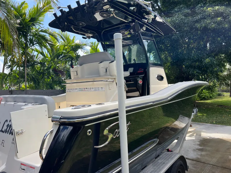 Slide: The Image of 2019 Scout 255LXF boat on trailer, black hull, outdoor setting with trees. - 4