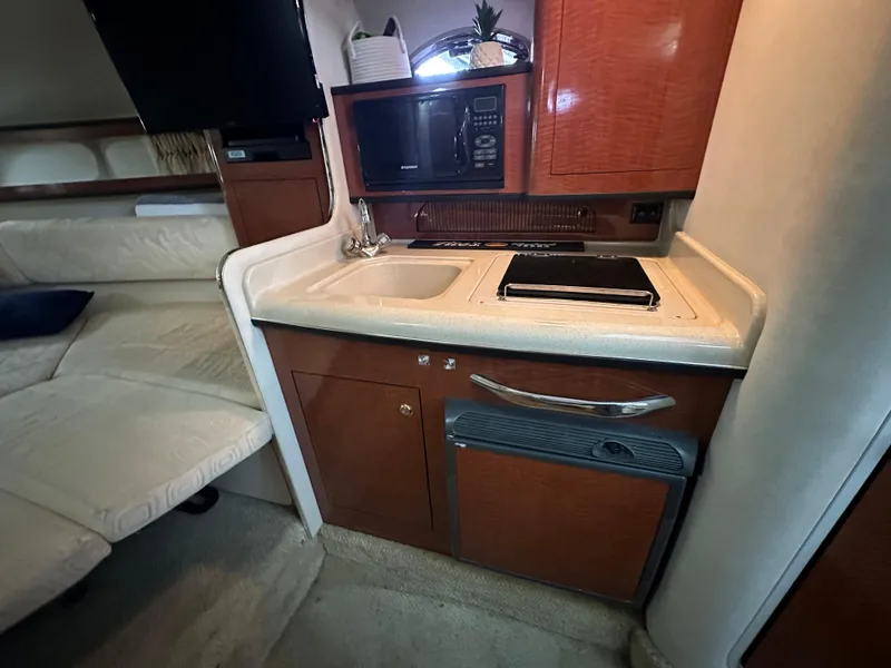 Slide: The Image of 2003 Sea Ray 280 Sundancer interior kitchen with sink, stove, microwave, and cabinetry. - 18