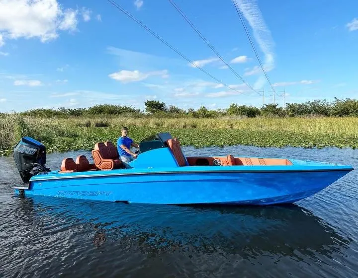 Slide: The Image of 2024 Concept 27' CC boat in blue on a calm waterway with lush greenery. - 2