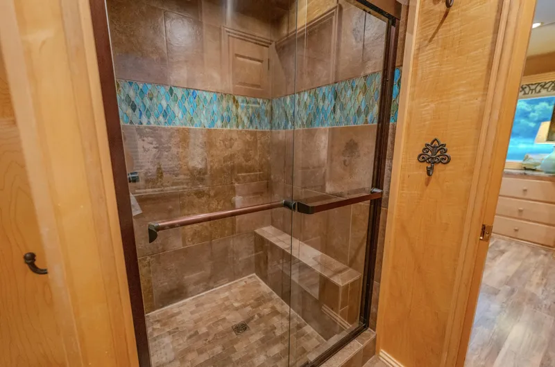 Slide: The Image of Luxurious glass shower with bench, decorative tile accents, and wooden surroundings in a modern bathroom. - 18