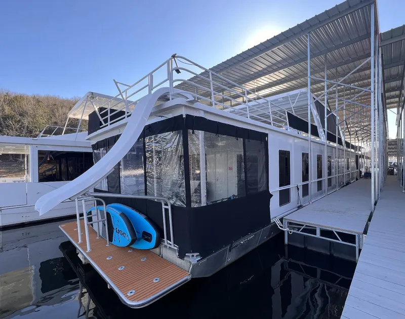 Slide: The Image of 2007 Fantasy 19 X 90 houseboat with slide and paddleboards docked under a covered marina. - 5