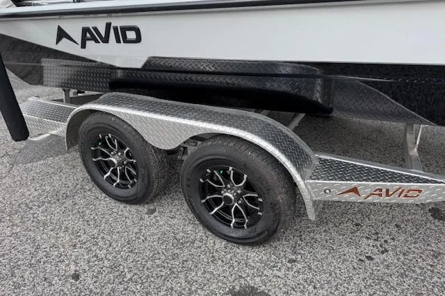 Slide: The Image of 2024 Avid 23 Fusion boat trailer with dual wheels on a textured surface. - 16