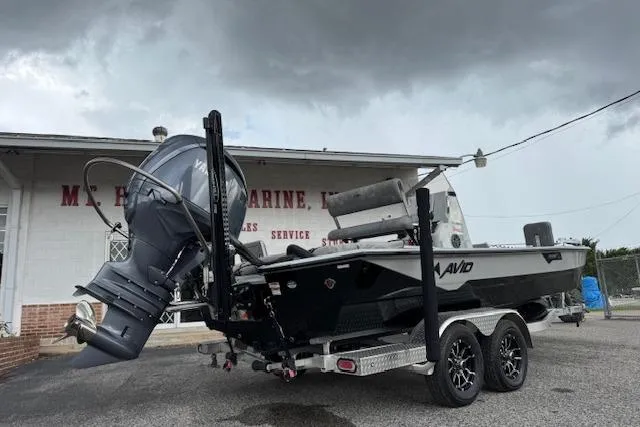 Slide: The Image of 2024 Avid 23 Fusion boat on trailer, parked outside marine service building under cloudy sky. - 3
