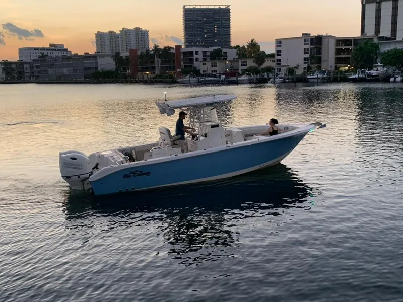Slide: The Image of 2019 Sea Chaser 27 HFC boat on calm water at sunset, urban skyline background. - 2
