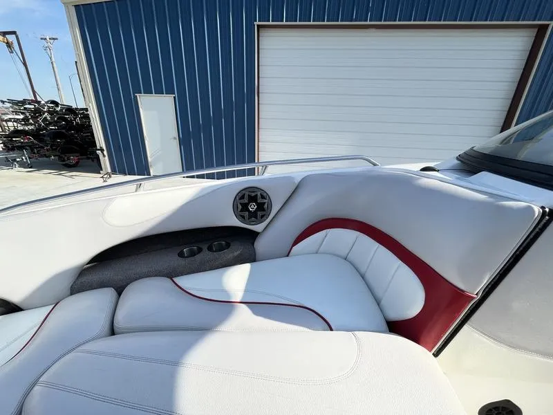 Slide: The Image of 2006 Malibu 23 LSV boat interior with white and red seating, docked near blue building. - 11
