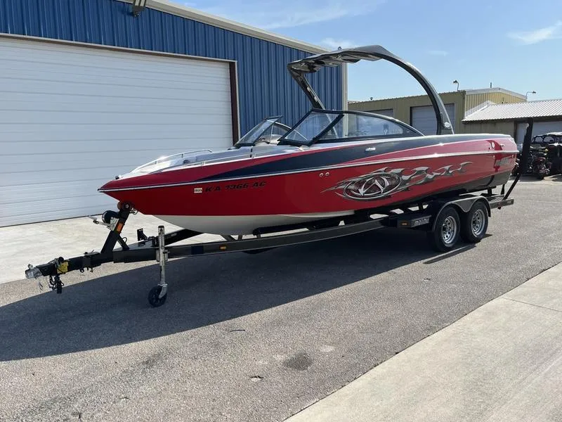 Slide: The Image of 2006 Malibu 23 LSV red wakeboard boat on trailer outside blue warehouse. - 2