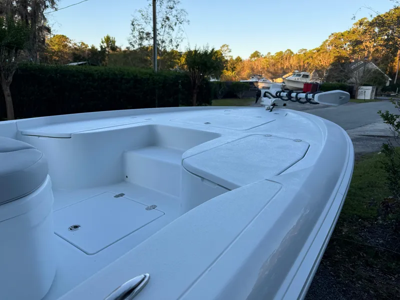 Slide: The Image of 2024 Contender 23 Bay boat, white deck, parked outdoors, surrounded by trees. - 11