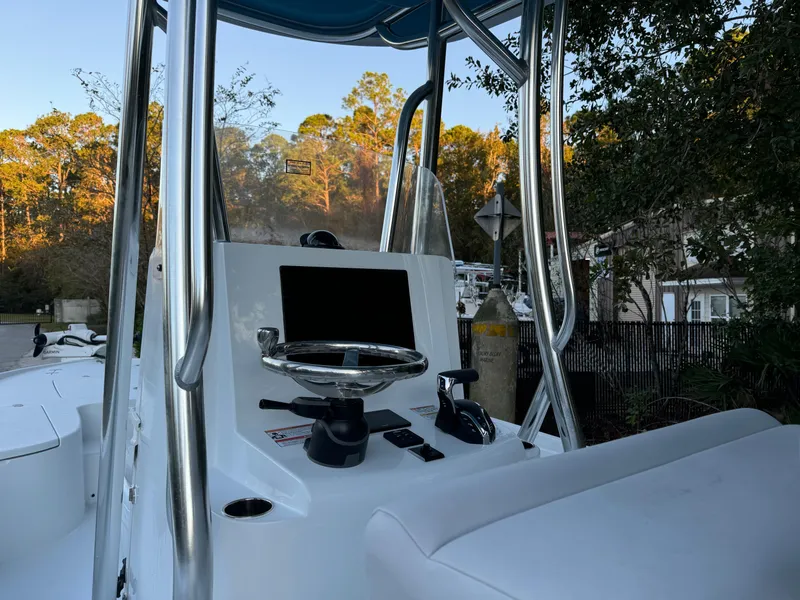 Slide: The Image of 2024 Contender 23 Bay boat console with steering wheel and controls, surrounded by trees. - 9