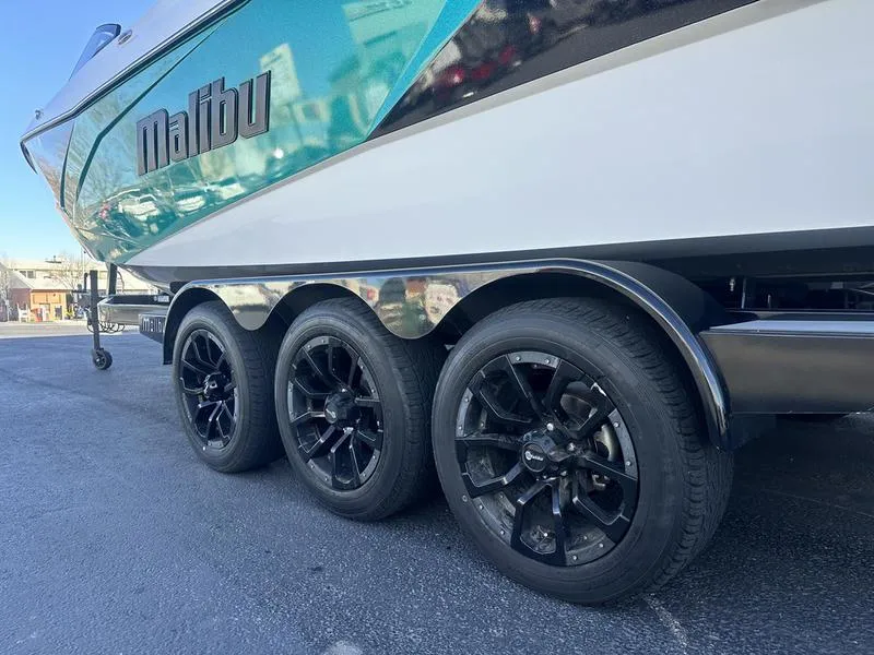 Slide: The Image of 2023 Malibu 26 LSV boat on triple-axle trailer with black wheels. - 5