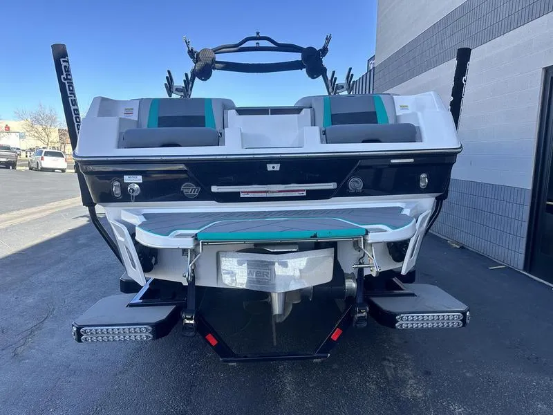 Slide: The Image of 2023 Malibu 26 LSV boat rear view with teal accents, parked outdoors. - 6