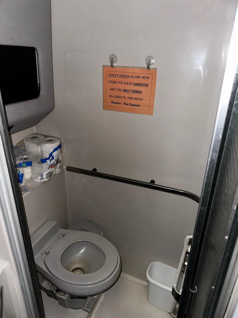 Slide: The Image of 1987 Sea Ray 460 Convertible bathroom with toilet, toilet paper, and caution sign. - 37