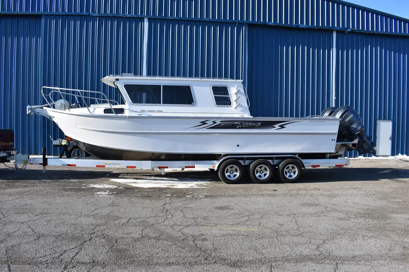 The Image of 2025 Weldcraft 280 Cuddy King T250XCB boat on trailer, parked outside blue warehouse. - 0