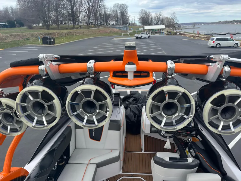 Slide: The Image of 2013 Nautique G23 boat with tower speakers and orange accents in a parking lot near a lake. - 8