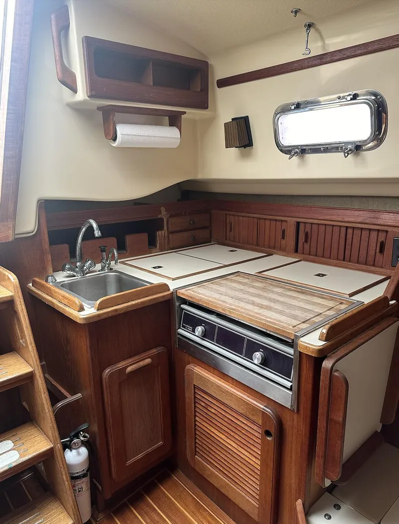 Slide: The Image of 1990 Island Packet 27 sailboat galley with wood cabinetry and stainless steel sink. - 14