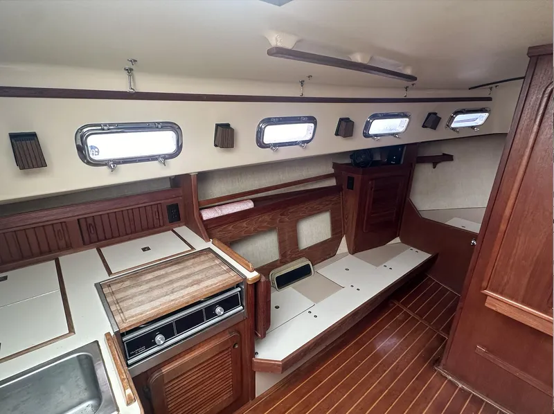 Slide: The Image of Interior of a 1990 Island Packet 27 sailboat, featuring wood finishes and compact kitchen area. - 15