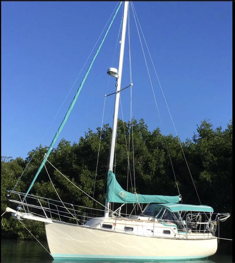Slide: The Image of 1990 Island Packet 27 sailboat with teal accents, docked near lush greenery. - 2