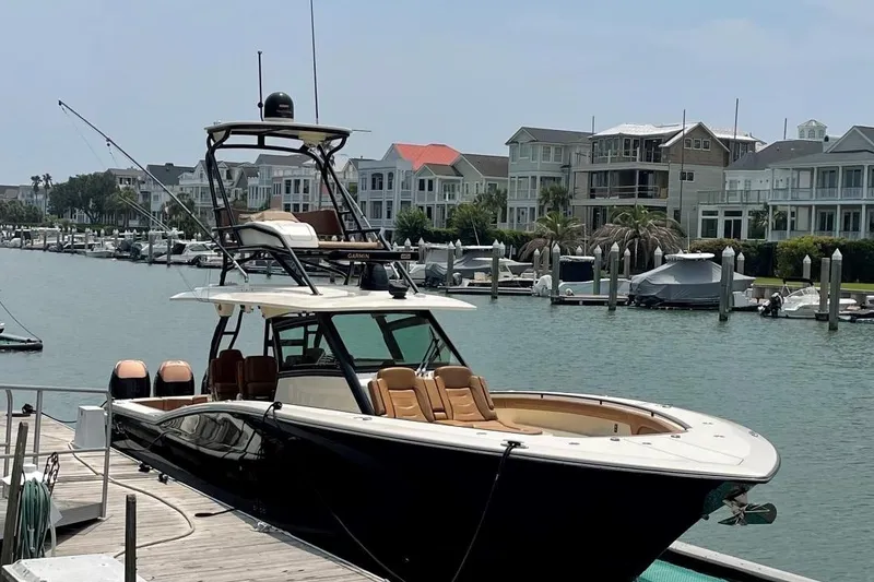 Slide: The Image of 2020 Scout 420 LXF luxury boat docked in a marina with waterfront homes. - 0