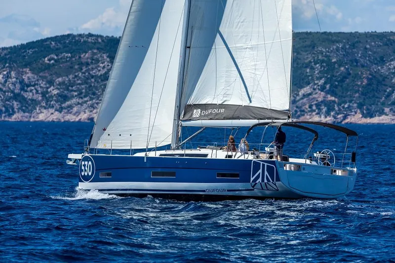 Slide: The Image of 2024 Dufour 530 sailboat cruising on open sea with scenic coastal backdrop. - 11