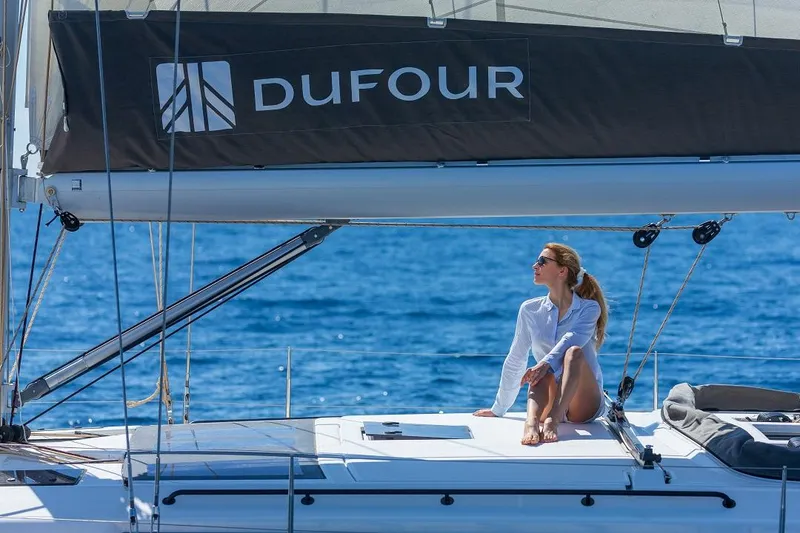 Slide: The Image of Woman relaxing on a 2024 Dufour 530 sailboat under clear blue skies. - 12